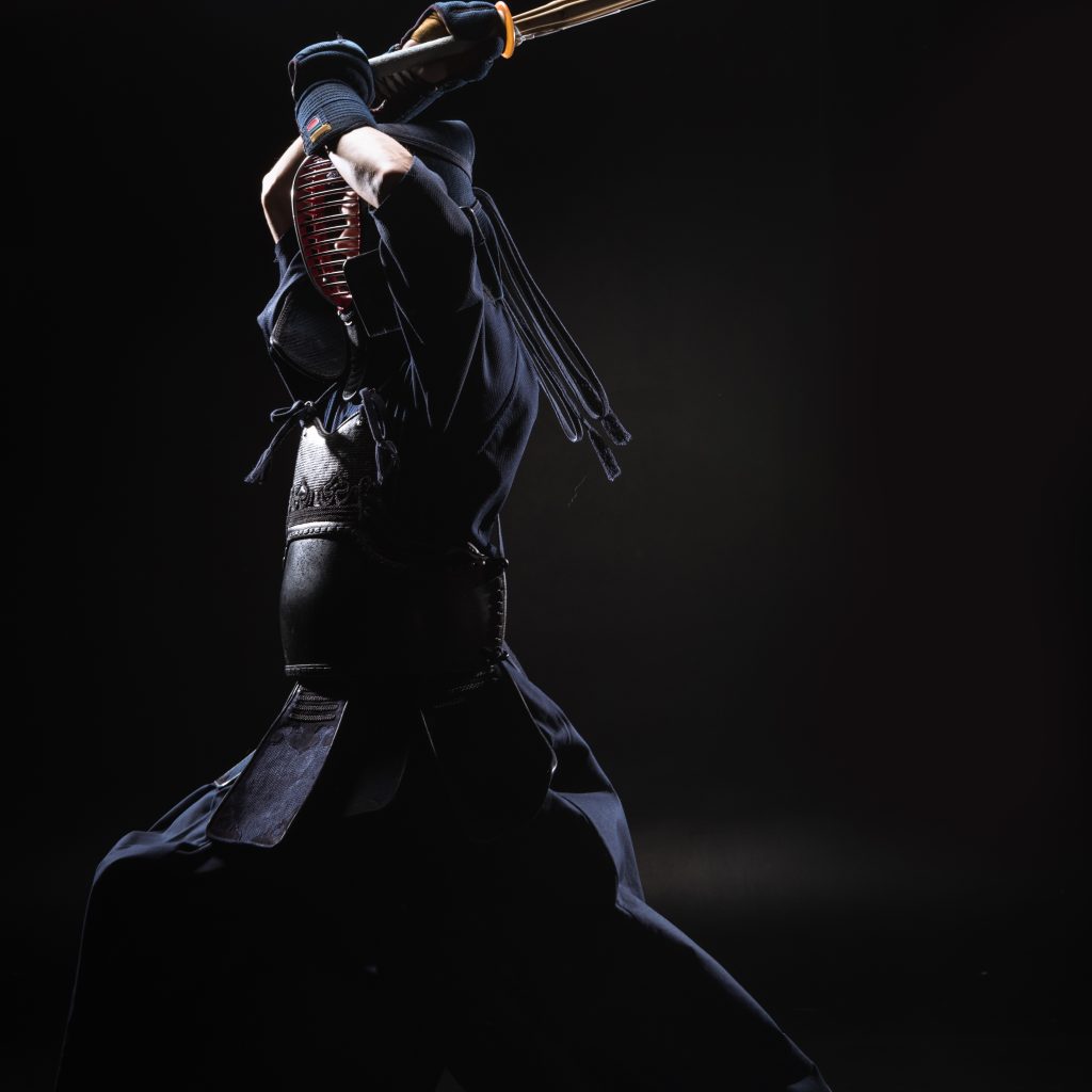Full length view of kendo fighter in armor practicing with bamboo sword on black